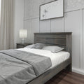 Neutral modern bedroom with gray wooden bed frame, white and gray bedding, bedside lamp on wood nightstand, framed dandelion wall art and board-and-batten paneling