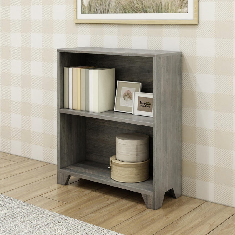 Gray wooden bookshelf with two shelves, holding books and decorative items, against a plaid patterned wall on a hardwood floor.