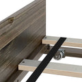 Close-up of wooden bed frame plywood slats with black metal center support strap and caster wheel under middle support near rustic wooden headboard
