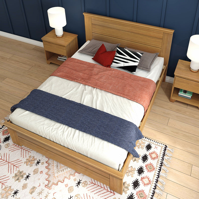 Oak platform bed with matching nightstands, layered blankets and accent pillows on patterned rug, navy blue accent wall