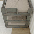 Top-down view of rustic gray wooden bunk bed safety guardrail with beige mattress and textured bedding on hardwood floor and rug