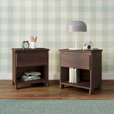 Children's bedside tables with white lamp, green alarm clock, pencil holder and wooden toy camera against soft green gingham wallpaper