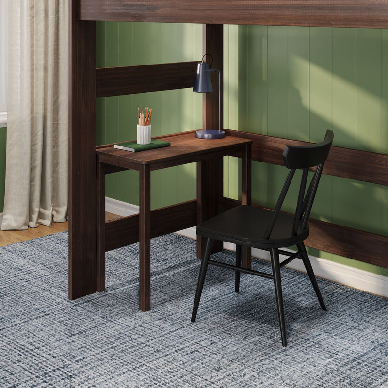 Wooden loft bed with built-in desk in a cozy green-paneled home office nook, navy task lamp, pencil holder on a notebook and black chair on a textured gray rug.