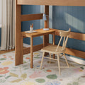 Kids loft bed study nook with wooden desk and chair, blue paneled wall, white desk lamp, pencil cup and pastel floral rug