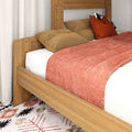 Cozy bedroom corner with solid oak bed frame, rust-orange quilt and pillows, patterned boho rug and neutral curtains