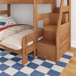 Solid wood twin-over-twin bunk bed with storage staircase and built-in drawers, beige bedding and car-print pillows on blue checkered rug in kids' bedroom