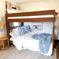 Wooden bunk bed in coastal-style bedroom with white comforter, blue striped pillows, plush blue throw and wicker accent decor