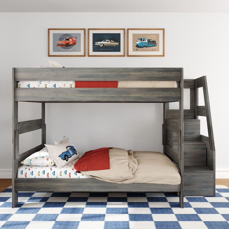 Gray wooden twin-over-full bunk bed with staircase storage, car-themed bedding and pillows, red throw blanket, framed vintage car prints, and blue-and-white check rug in a modern kids' bedroom