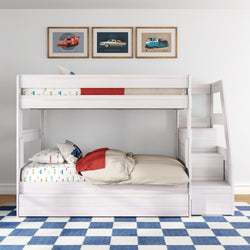 White wooden twin-over-full kids bunk bed with staircase and built-in storage, car-themed bedding and pillows, blue checkered rug and framed vintage car prints in a modern children's bedroom