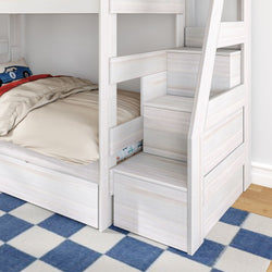 White wooden bunk bed with built-in storage stairs and pull-out drawers, beige bedding and blue checkered rug in kids' bedroom