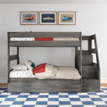 Gray wooden kids loft bunk bed with stairs and storage, car-print bedding and pillows, blue-and-white checkered rug and three framed vintage car posters above