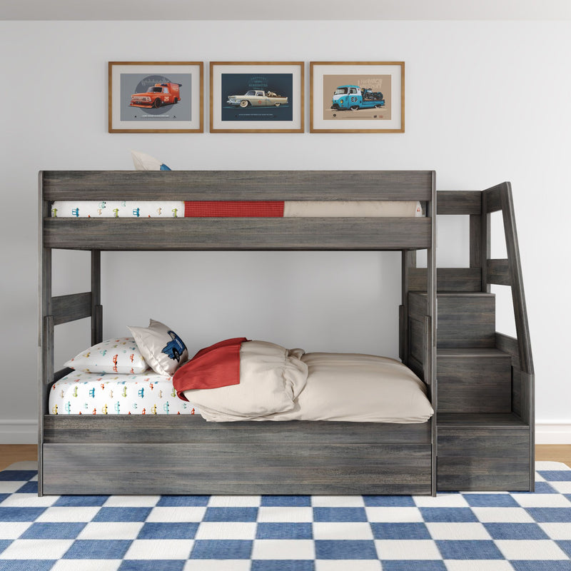 Gray wooden kids loft bunk bed with stairs and storage, car-print bedding and pillows, blue-and-white checkered rug and three framed vintage car posters above