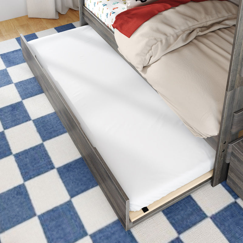 Children's wooden twin trundle bed with pull-out white mattress, beige bedding and red throw on blue checkered rug