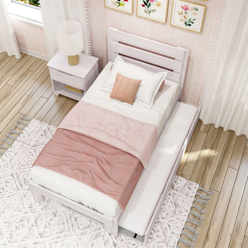 Pastel pink girls' bedroom with white wooden twin bed, blush duvet and textured pillow, white nightstand with lamp, floral wall art and boho rug