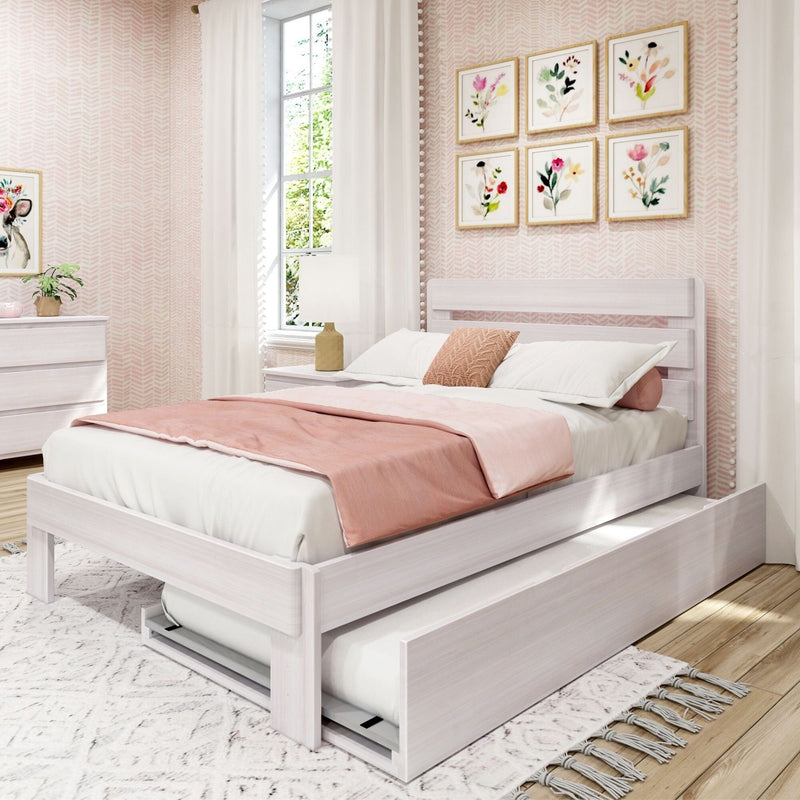 White wooden platform bed with pull-out trundle and blush pink bedding in a bright girls' bedroom with floral wall art, white curtains, bedside lamp, and matching dresser
