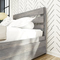 Close-up of modern gray wood bed frame headboard with white bedding, chevron wallpaper accent, bedside lamp and hardwood floor