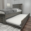 Gray wooden platform bed with pull-out trundle mattress, space-saving storage bed frame in modern rustic bedroom with bedside lamp