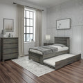 Rustic gray wooden twin bed with pull-out trundle and matching dresser and nightstand in modern farmhouse bedroom with black-framed window, neutral curtains, hardwood floors, table lamp and patterned area rug