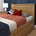 Modern oak bed frame with storage drawers, paneled headboard, coral quilt, red accent pillows and white bedside lamp