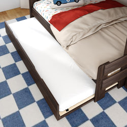 Wooden trundle bed with pull-out twin mattress under a kids bed, beige bedding and car-print pillow on a blue checkered rug