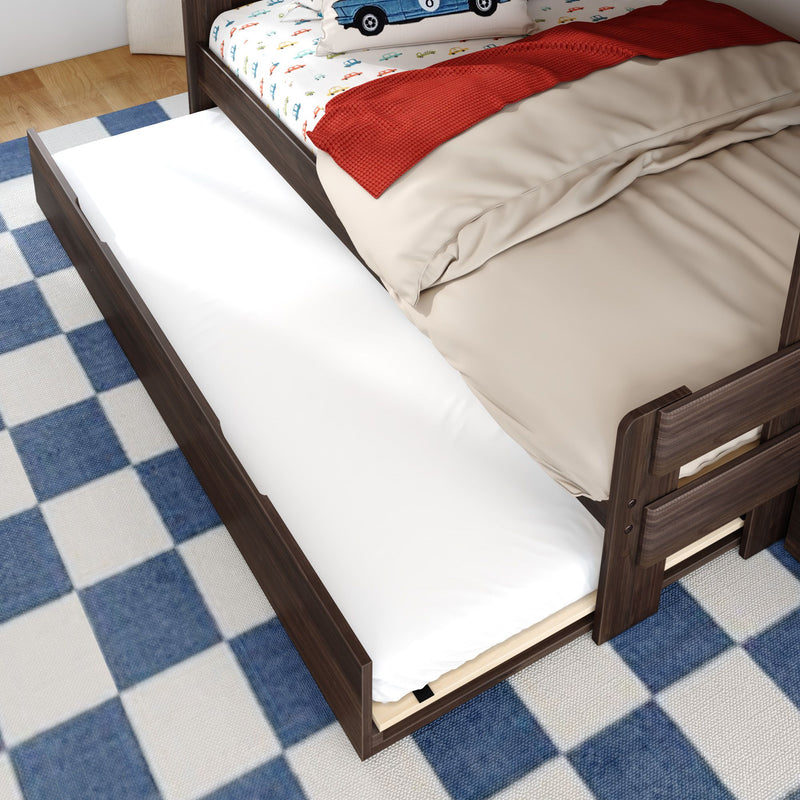 Wooden trundle bed with pull-out twin mattress under a kids bed, beige bedding and car-print pillow on a blue checkered rug