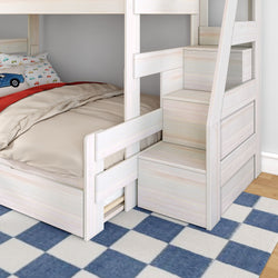 Whitewashed wooden twin-over-twin bunk bed with built-in storage stairs and drawers, beige bedding and car-print pillows on blue check rug, space-saving kids' bedroom furniture