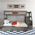 Gray wood kids bunk bed with stairs and storage, car-themed bedding and pillows, framed vintage car prints above and blue checkered rug