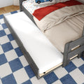 Gray wood kids trundle bed with pull-out mattress, car-print sheets, red throw blanket and blue check rug