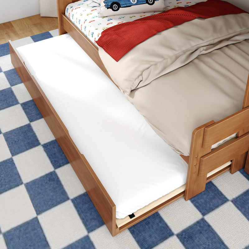 Wooden kids trundle bed with pull-out mattress, car-print sheets, beige duvet and red textured throw on a blue checkered rug — children's bed with under-bed storage