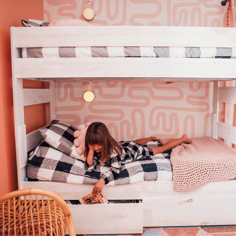 Child reading a book on a cozy bunk bed with pink and gray decor in a modern children's bedroom.