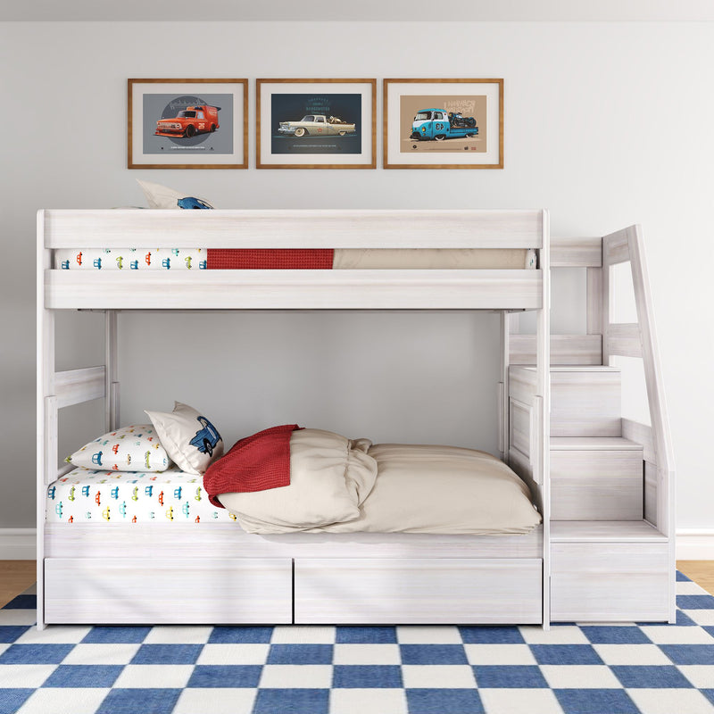 White wooden bunk bed with staircase in kids bedroom, car-themed sheets and pillows, vintage car framed prints above, under-bed storage drawers on blue checkered rug
