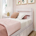 Cozy modern bedroom with blush pink bedding, textured knit throw pillow, white wooden storage bed with drawers, bedside lamp and floral wall art
