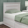 Whitewashed wood twin bed with paneled headboard and under-bed storage drawers, green pillow and quilt, matching nightstand and lamp in a modern bedroom