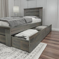 Gray wooden storage bed with open under-bed drawers, gray bedding and pillows, nightstand with lamp in a modern minimalist bedroom with hardwood floors and paneled wall