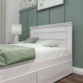 Modern bedroom close-up with whitewashed wood bed frame, sage green board-and-batten accent wall, green bedding and bedside lamp