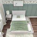 Overhead view of bedroom with green board-and-batten accent wall, leaf-pattern wallpaper, whitewashed twin bed with green bedding, nightstand and lamp