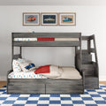 Kids' grey wooden bunk bed with staircase and built-in storage drawers, car-themed bedding and pillows, framed vintage car prints on white wall and blue checkered rug