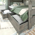 Grey wood platform bed with built-in under-bed storage drawers pulled out showing pillows and linens, green duvet and patterned throw pillows in a modern farmhouse bedroom