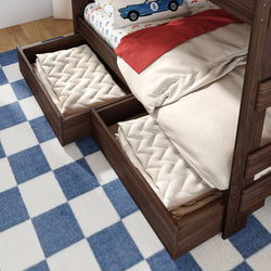 Walnut wooden bunk bed with pull-out under-bed storage drawers holding folded cream quilts, beige bedding, red throw and car-print pillow on blue checkered rug