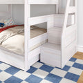White wooden twin bunk bed with built-in storage staircase and drawers, beige bedding and kids car pillow on blue checkered rug in child's bedroom