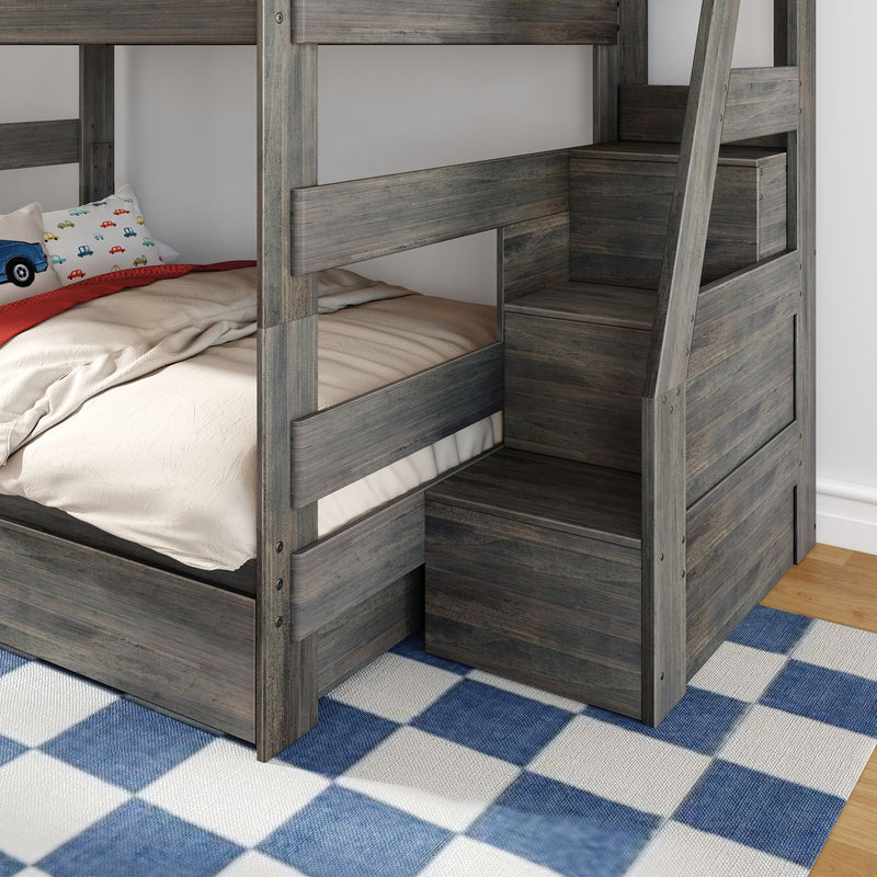 Grey wooden bunk bed with built-in staircase storage, beige bedding, car-print pillow and blue checkered rug in a kids' bedroom