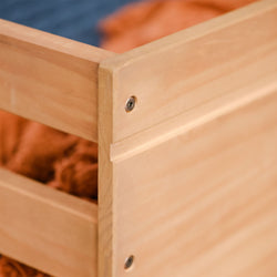 Close-up of light natural wood bed frame corner with recessed metal screws and orange bedding, modern wooden bedroom furniture detail