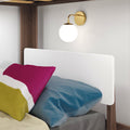 Brass globe wall sconce above bunk bed with wooden frame, white headboard and colorful pillows, modern bedside lighting
