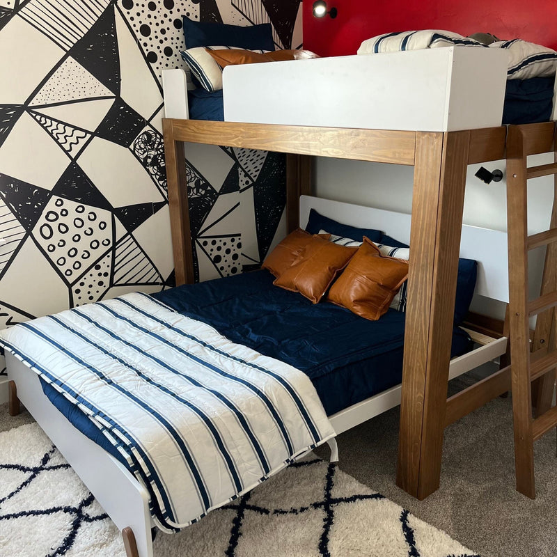 Wooden loft bunk bed with navy bedding, striped white quilt and brown leather pillows against geometric black-and-white accent wall