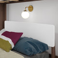 Modern brass wall sconce above white headboard in a minimalist bedroom with colorful pillows and navy duvet