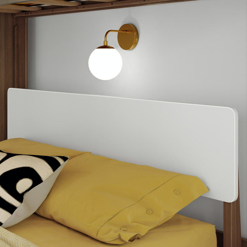 Close-up of modern bedroom with white rounded headboard, brass globe wall sconce, mustard-yellow bedding and black-and-white patterned accent pillow on wooden bed frame