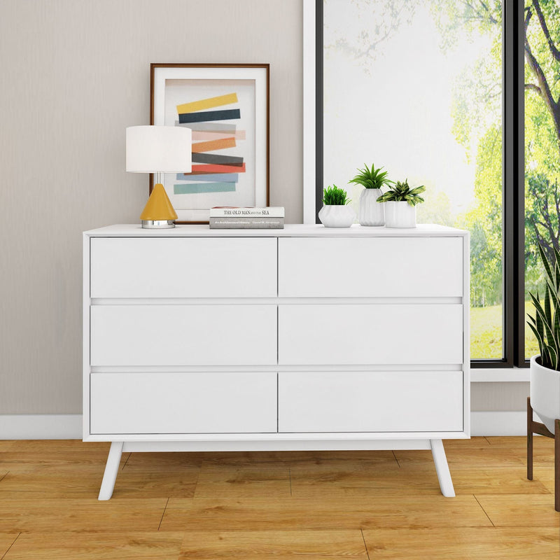 Modern white dresser with six drawers, topped with a lamp, book, and decorative plants in a stylish room with wooden floor and large window.