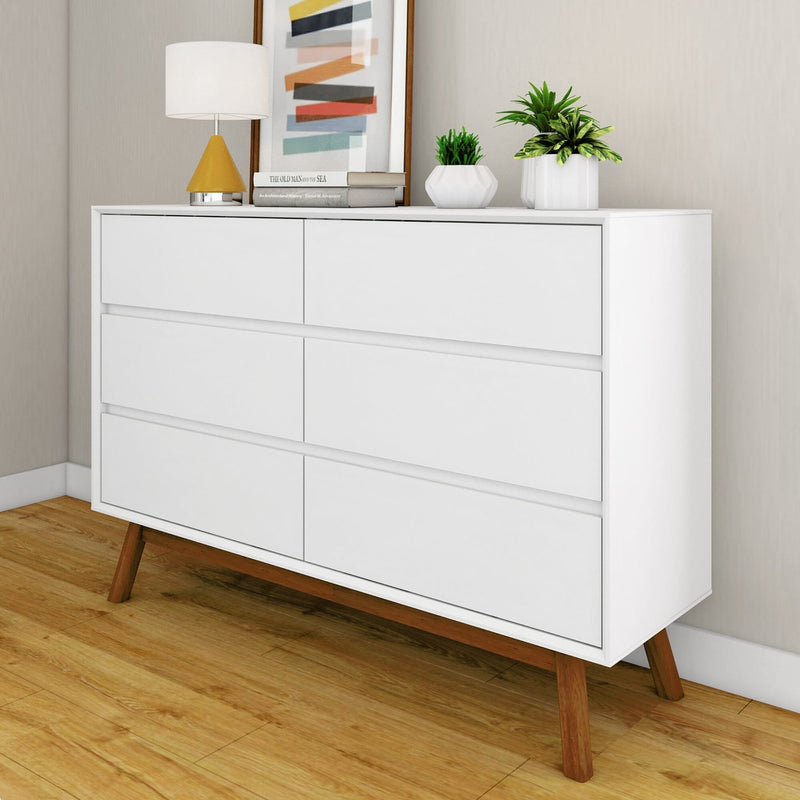 Modern white dresser with wooden legs, featuring decorative lamp and plants on top, against a light-colored wall.