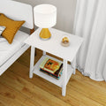 Modern white bedside nightstand with mustard yellow table lamp, glass decorative orb and stacked books next to a bed with mustard pillow on hardwood floor