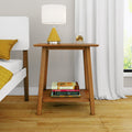 Mid-century modern wooden nightstand beside a white bed, topped with a white drum lamp with yellow cone base and glass orb, stacked books on the lower shelf, yellow pillows, hardwood floor and white curtains — stylish bedroom decor.